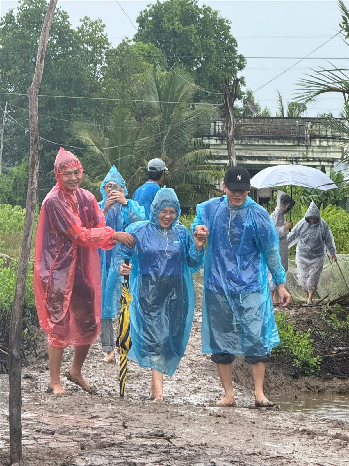 Các thành viên mặc áo mưa nắm tay nhau đi trên lối đất ướt